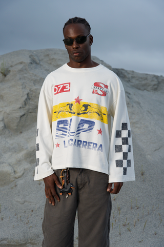 Modelo usando la camiseta La Carrera Longsleeve SALPI, vista de cuerpo completo con pantalones y estilo urbano inspirado en las carreras, look casual y cómodo