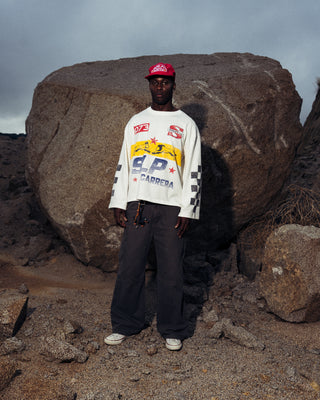 Modelo usando la camiseta La Carrera Longsleeve SALPI, vista de cuerpo completo con pantalones y estilo urbano inspirado en las carreras, look casual y cómodo